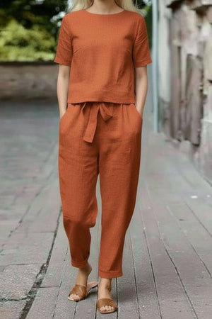 Woman wearing rust-colored cotton linen set with short-sleeve top and straight-leg pants outdoors