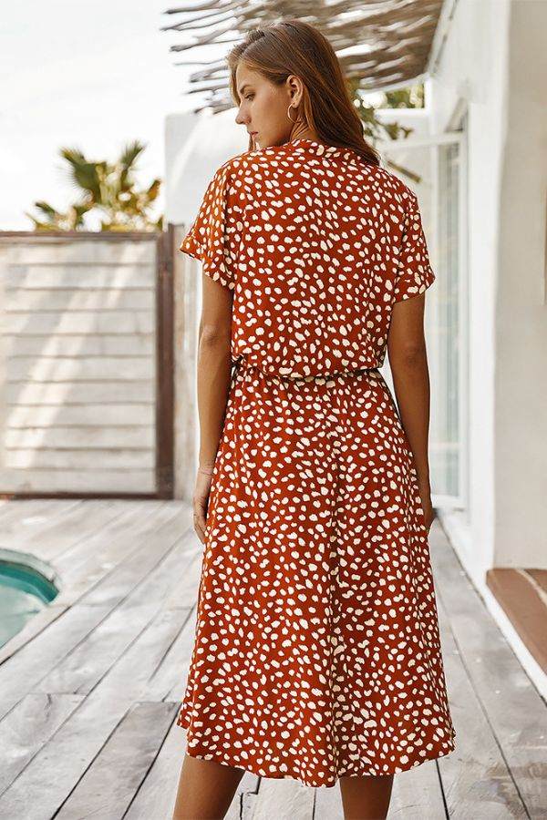 Woman wearing a casual bohemian dress skirt with white dot print and lace-up waist standing outdoors by a wooden deck