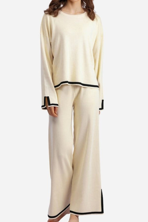 Woman wearing cream long sleeved relaxed fit lounge two-piece set with black trim on cuffs, hem, and pant edges