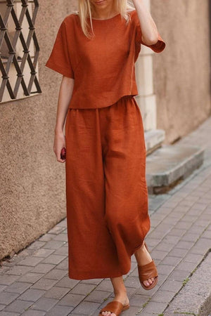 Woman wearing rust-colored loose fit co-ord set with short sleeves and wide-leg pants walking on a city sidewalk