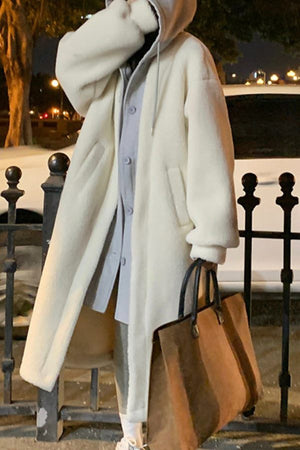 Woman wearing oversized white sherpa long coat with hood carrying brown tote bag at night outdoors