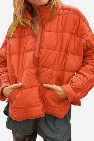 Orange lightweight puffer travel jacket with front pockets and half-zip closure worn by a model