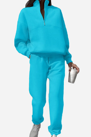 Woman wearing bright blue cotton-blended two-piece tracksuit with high collar and zipper, holding a coffee cup.