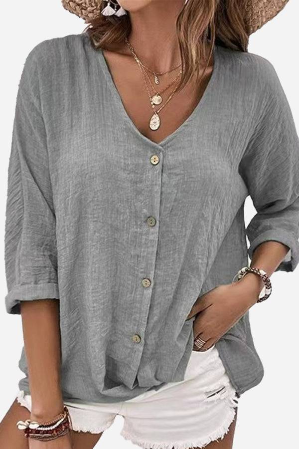 Gray button front tunic with crinkled fabric, V-neck, and rolled sleeves worn with white shorts.
