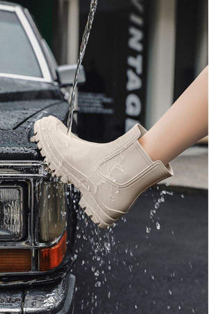 Light beige non-slip rain boots with SuperGrip sole being splashed with water, demonstrating waterproof feature.