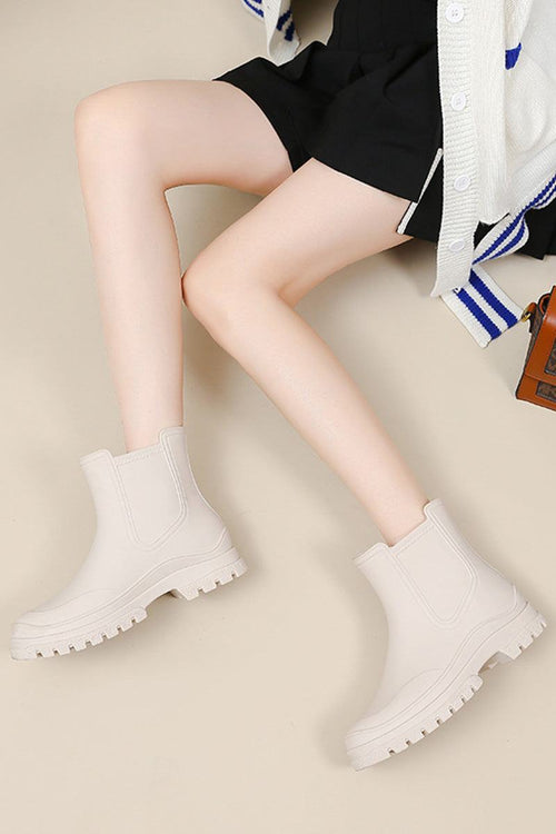 Light beige non-slip rain boots with chunky soles worn with black shorts and a white cardigan