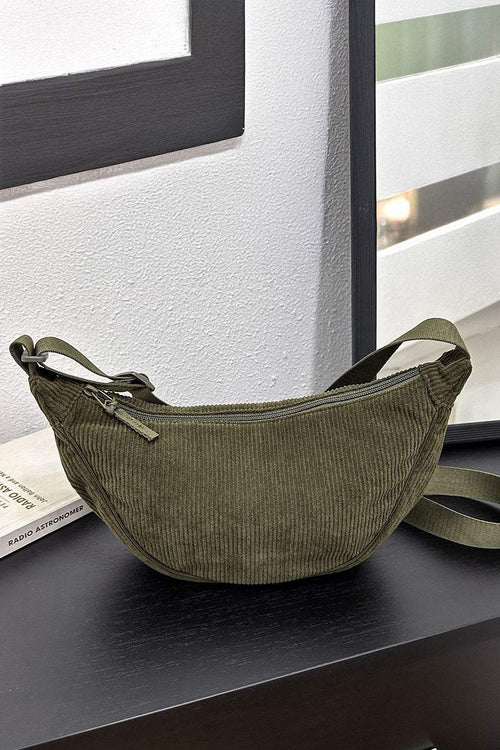 Olive green corduroy shoulder bag with adjustable strap and zip closure on black surface