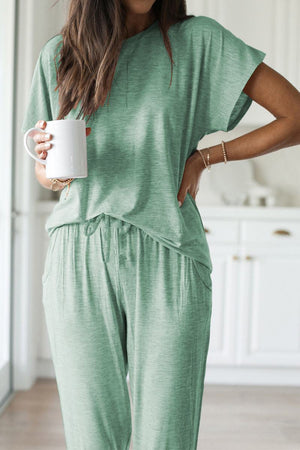Woman wearing green ultra-soft two-piece loungewear set with batwing sleeves and jogger pants holding a white mug indoors