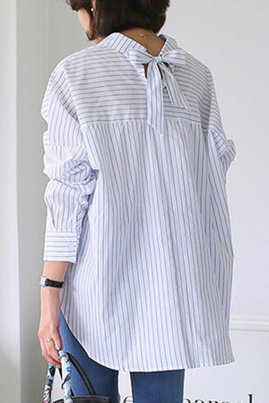 Back view of a woman wearing a 100% cotton oversized striped shirt with a bow detail at the neck and long sleeves.