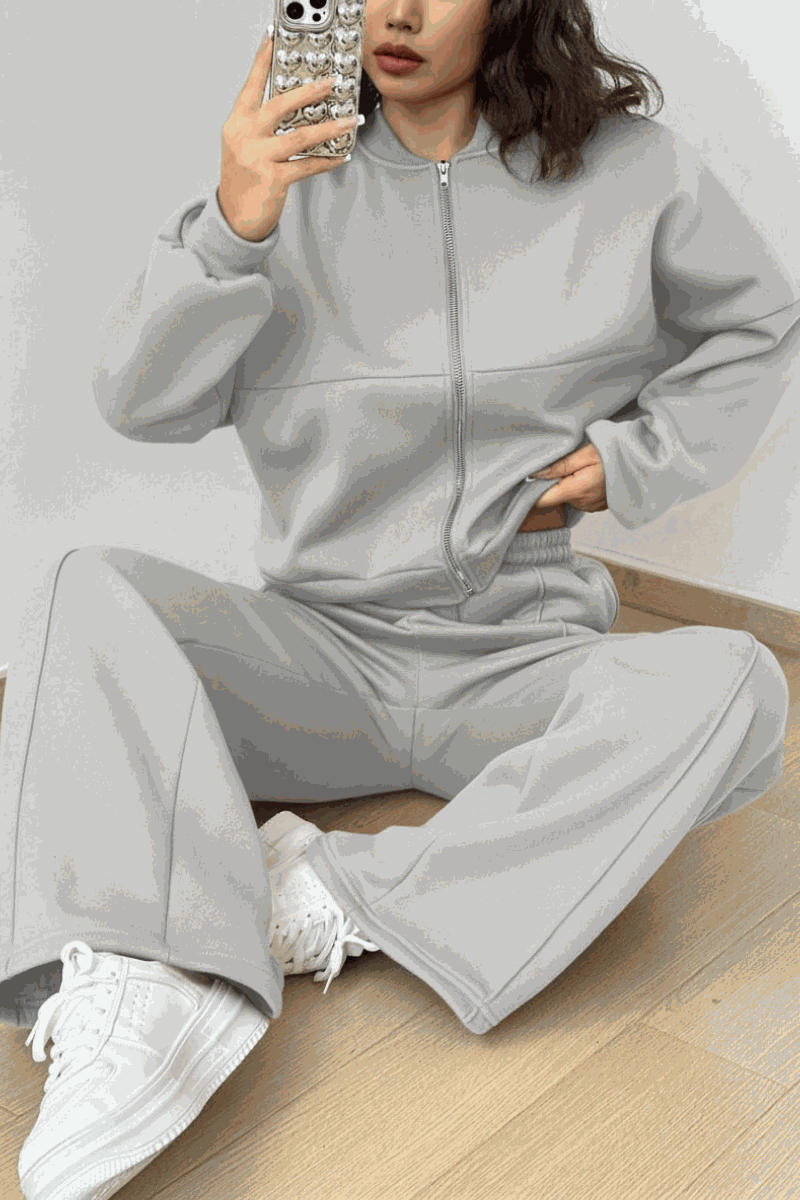 Woman wearing The Voyager Zip Set, light gray zip-front sweatshirt and wide-leg joggers with white sneakers, casual travel outfit