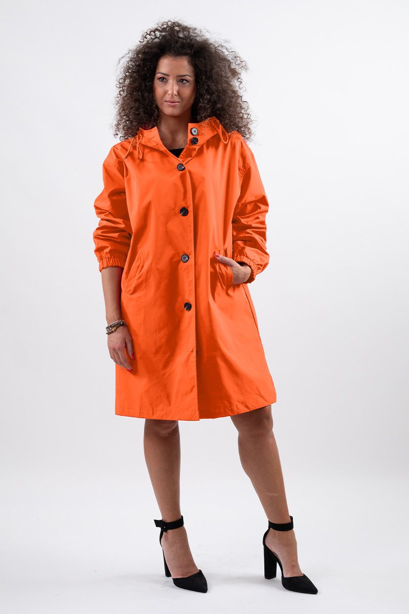 Woman wearing orange water resistant oversized windbreaker with hood and buttons