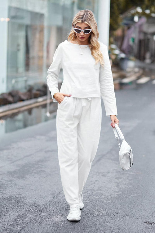 Woman wearing cotton-linen monochrome relaxed longline top and wide-leg pants set walking outdoors with sunglasses and white handbag