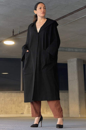 Woman wearing black oversized water resistant windbreaker jacket with hood and snap-button closure indoors