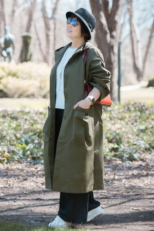 Woman wearing oversized olive green water resistant windbreaker jacket with hood and large pockets outdoors