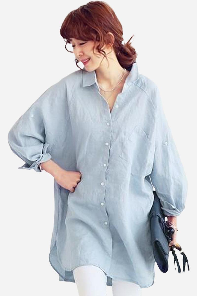 Woman wearing a light blue oversized linen shirt with long sleeves and buttons, styled casually with white pants and holding a black clutch.