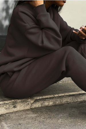 Woman wearing a dark brown cotton blend tracksuit sitting on concrete steps, showing relaxed fit and soft texture.