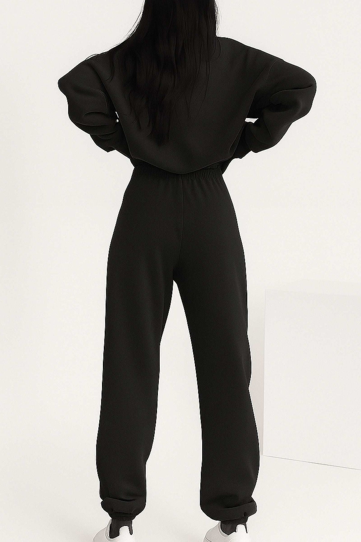 Back view of woman wearing black cotton blend tracksuit with stretch waistband and cuffs, showcasing relaxed fit and minimalist style.
