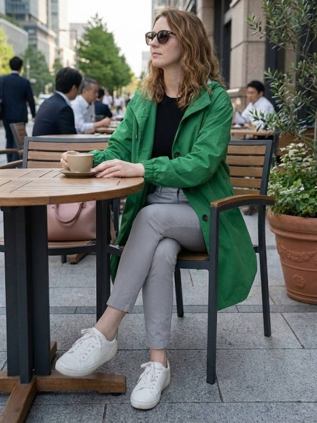 Woman wearing green Rain Couture Windbreaker sitting at outdoor cafe table drinking coffee