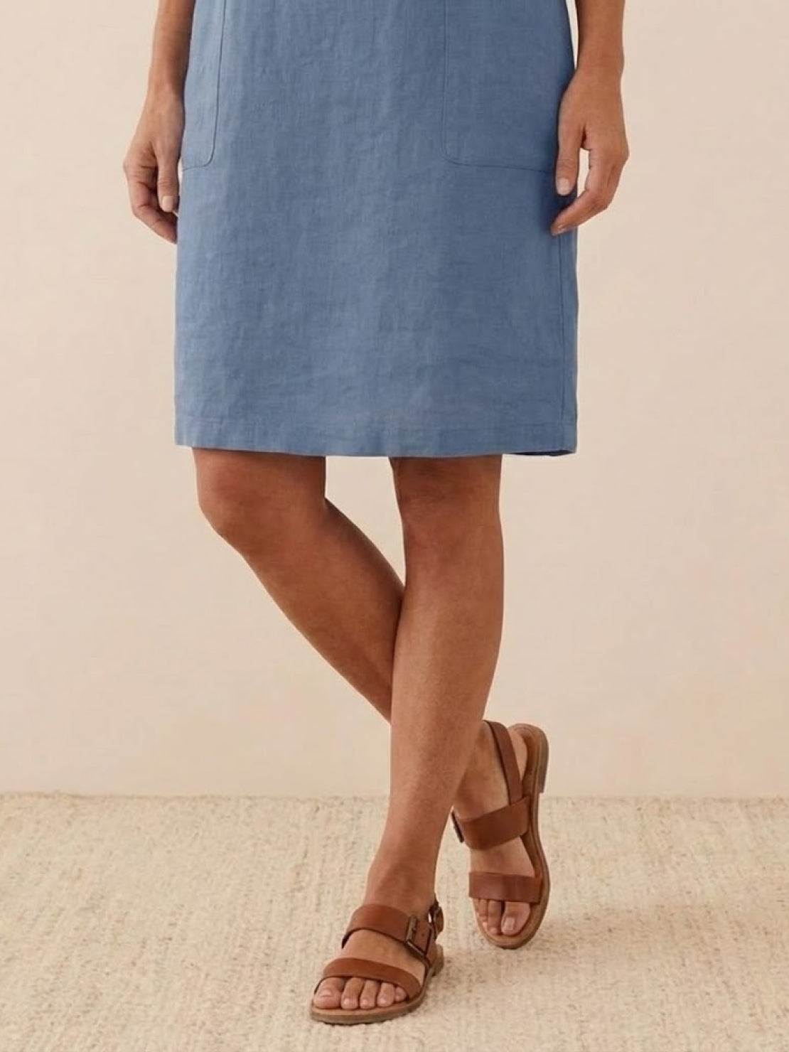 Woman wearing blue cotton dress and brown sandals standing on wooden floor