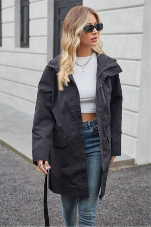 Woman wearing a black water-resistant windbreaker trench jacket with belt over casual outfit outdoors