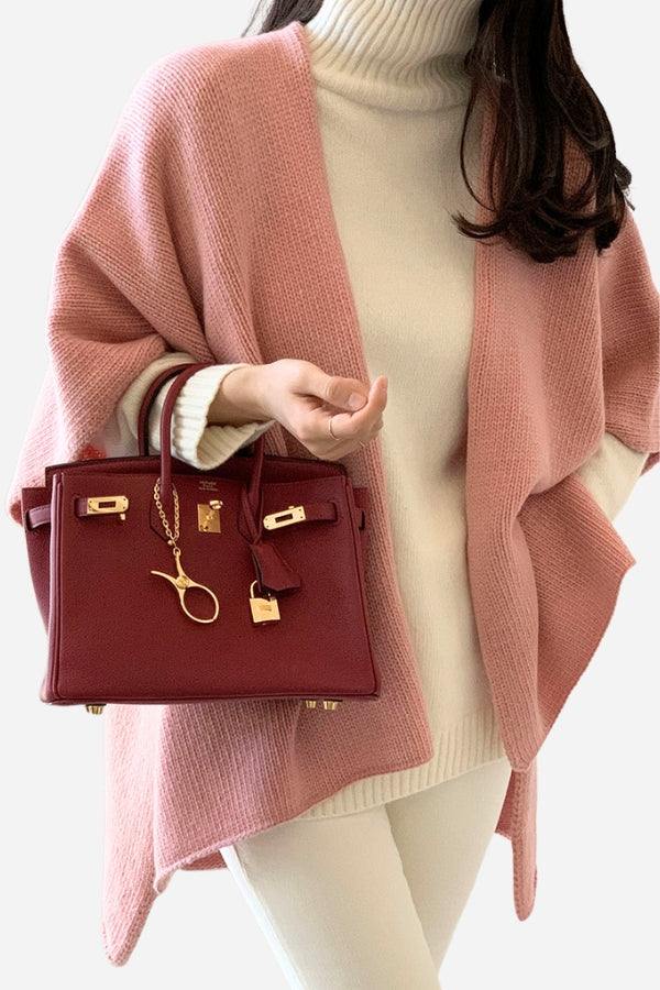 Woman wearing relaxed flowy open front knitwear cardigan in pink with white turtleneck and pants, holding a maroon handbag