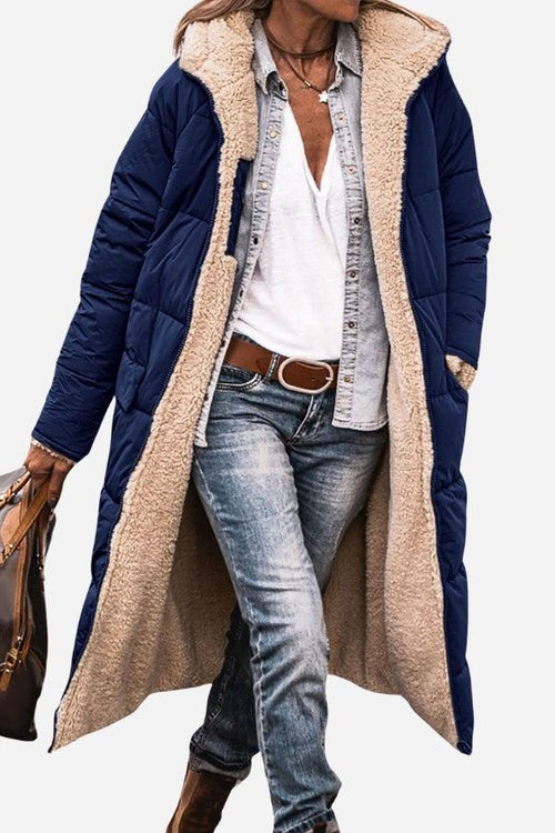 Woman wearing navy Sherpa-lined hooded teddy coat with plush beige interior and pockets, styled with jeans and casual shirt