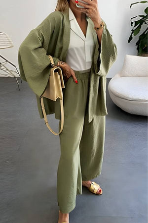 Woman wearing a chic comfort kimono two-piece set in olive green, styled with a white blouse and beige handbag in a modern living room.