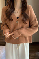 Woman wearing soft brown casual loose boxy cardigan with buttons over a black top and white pants