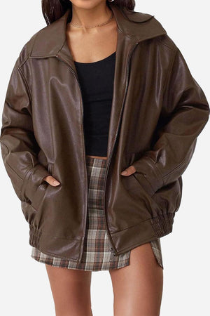 Oversized faux leather brown motorcycle jacket with zip closure and pockets worn over black top and plaid skirt