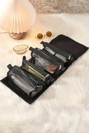 Compact black nylon travel makeup bag with multiple compartments and zipper pockets for organized cosmetics, laid open on a white furry surface next to sunglasses and lamp, designed for travel light look right.
