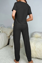 Woman wearing black My Go To Loungewear two-piece set standing in cozy bedroom setting