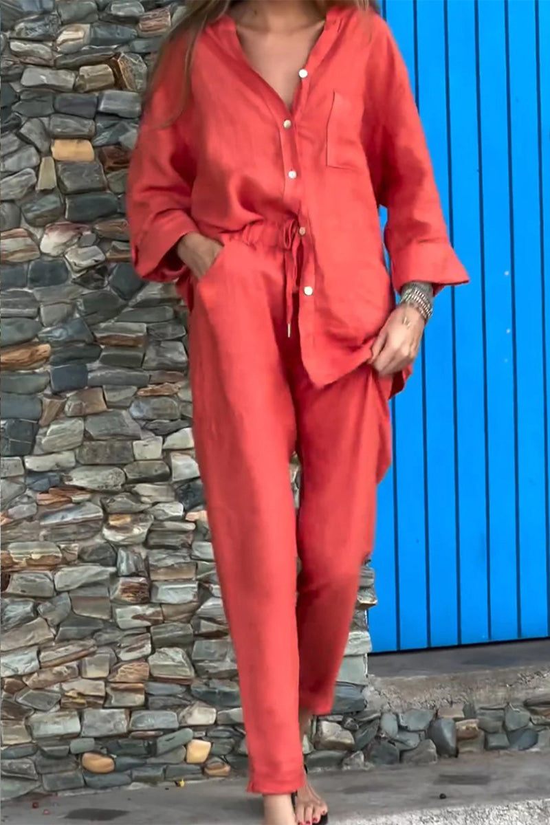 Woman wearing bright red casual chic two-piece set with relaxed fit and button-up top standing by stone wall and blue door