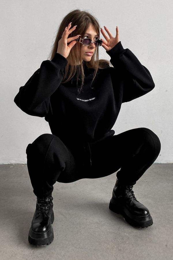 Woman wearing black Storm Sweater Mock Neck athleisure set with relaxed fit and boots against gray background