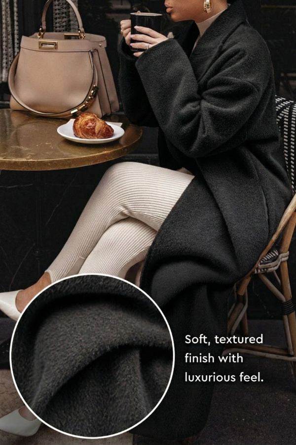 Black oversized teddy coat with soft textured fabric and relaxed fit worn by a seated woman at a café table.