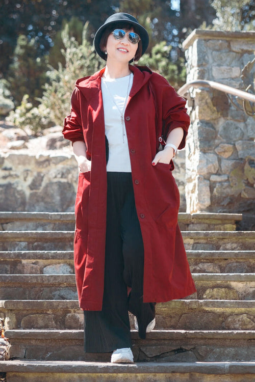 Woman wearing oversized one size fits all waterproof water-resistant red windbreaker jacket with hood outdoors on stairs