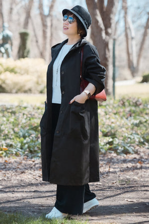 Woman wearing a black oversized waterproof windbreaker jacket with hood and snap-button closure outdoors
