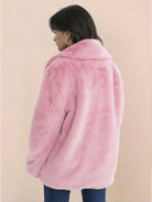 Back view of a woman wearing a soft pink open front oversized faux fur jacket with draped shawl collar and mid-hip length.