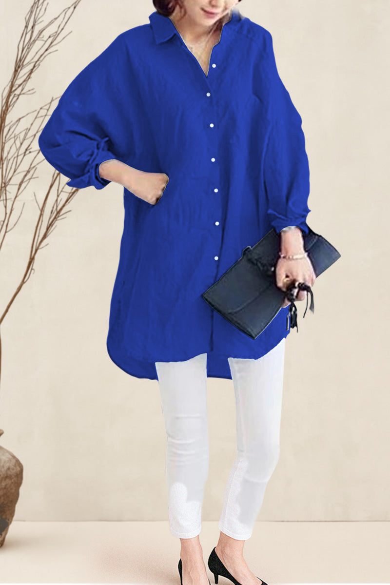 Woman wearing oversized linen shirt in blue with white pants and black heels, holding black clutch bag.