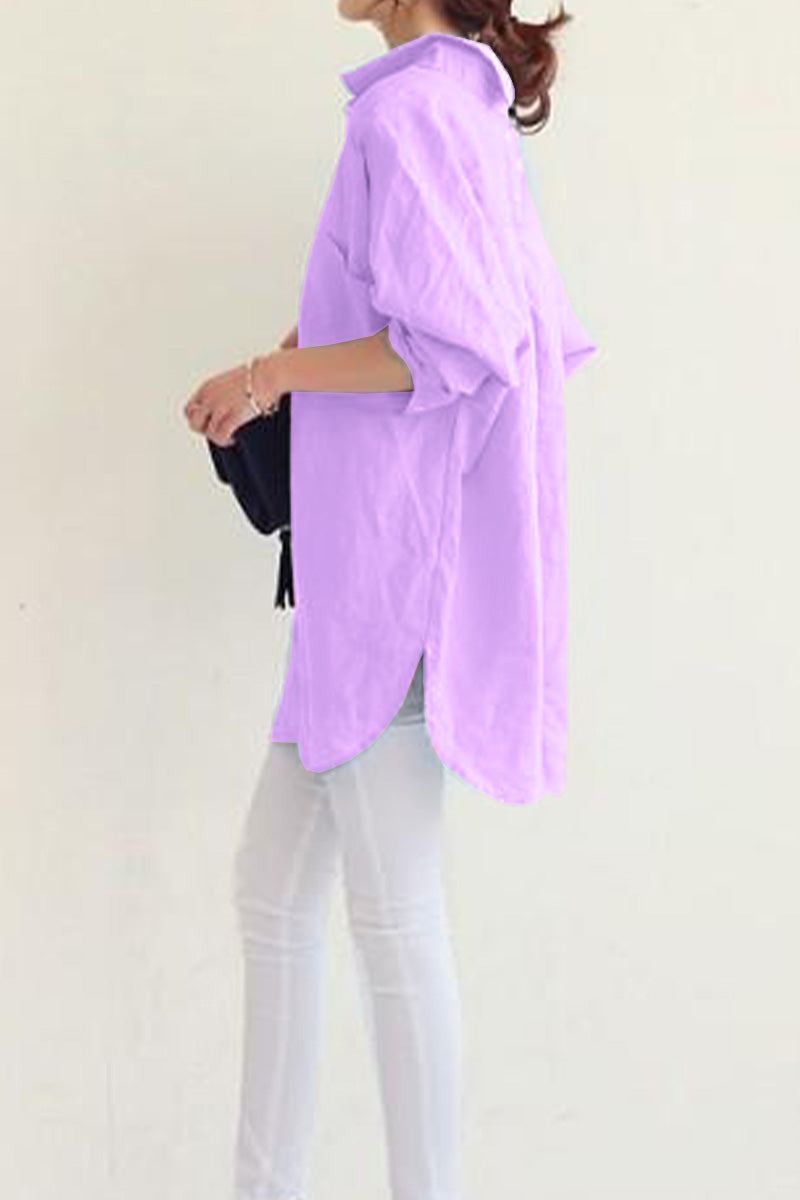 Woman wearing a light purple oversized linen shirt with rolled-up sleeves and white pants, side view
