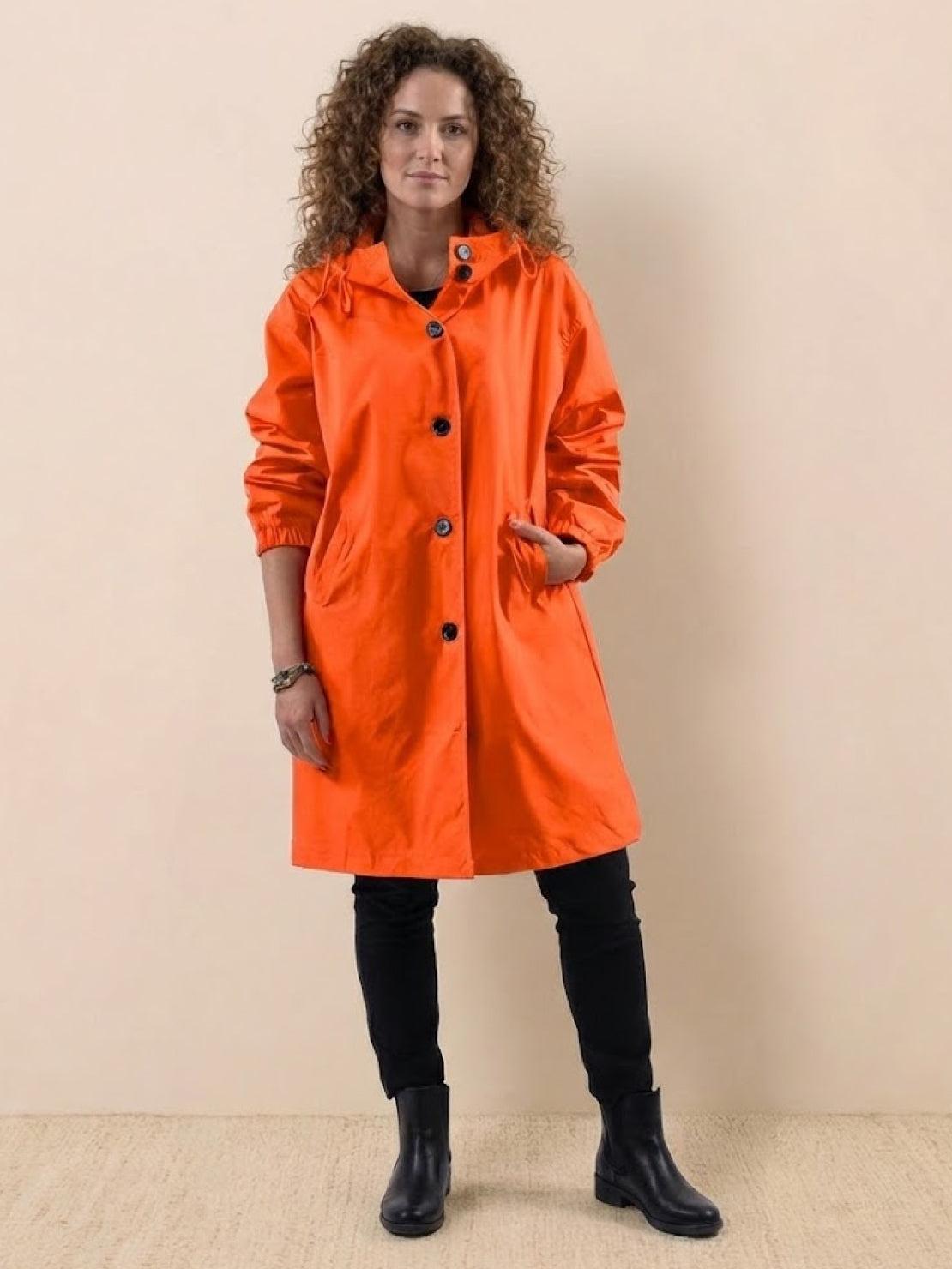 Woman wearing bright orange oversized Rain Couture Windbreaker jacket with black buttons, styling with black pants and boots