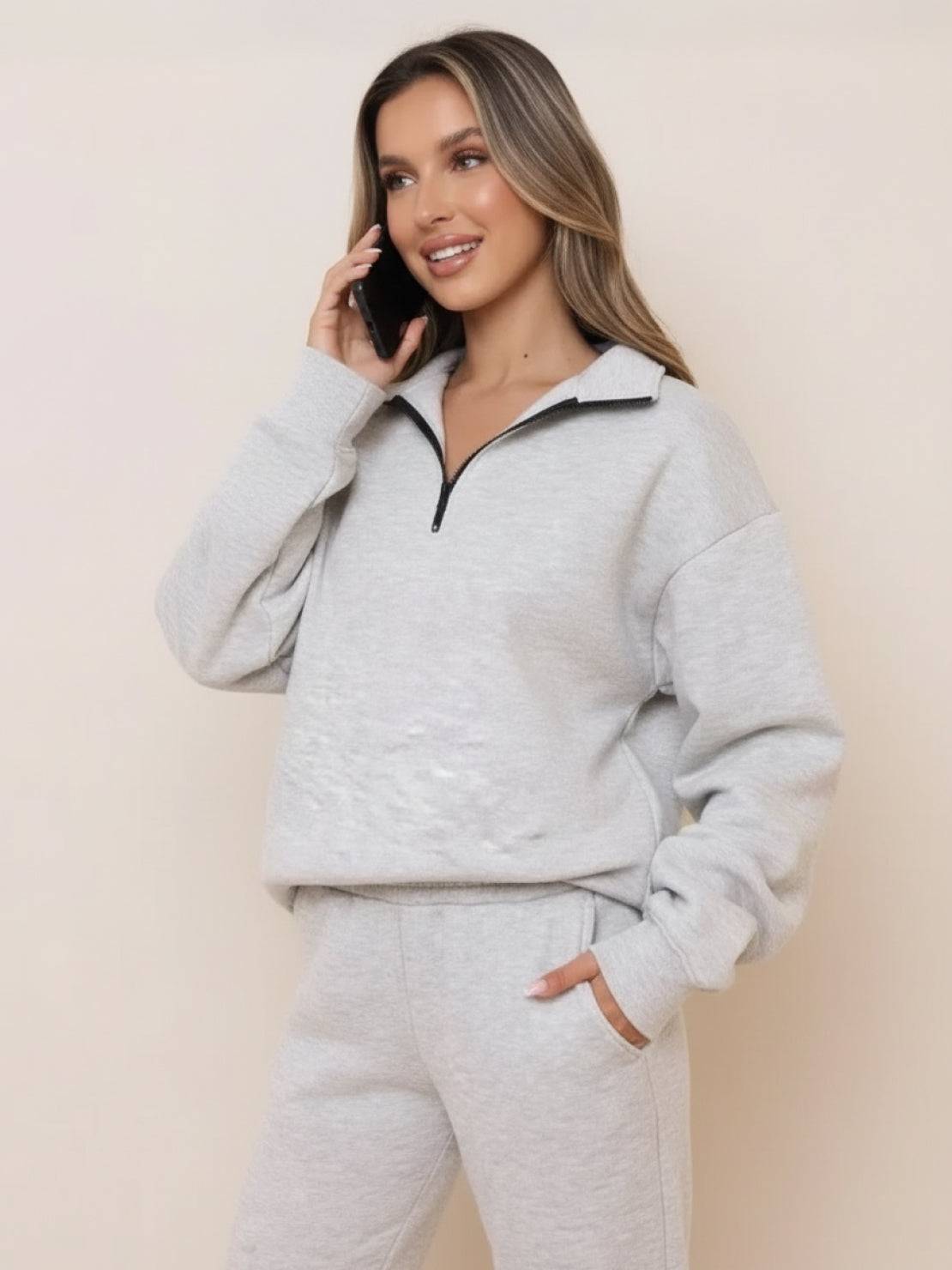Woman wearing light gray ultra-soft and comfy co-ord tracksuit set with zippered collar and pockets, talking on phone