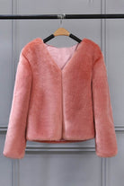 Pink bold faux fur jacket with V neckline and button front closure hanging on wooden hanger