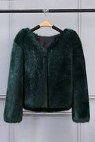 Dark green bold faux fur luxe jacket with V neckline and button closure hanging on wooden hanger